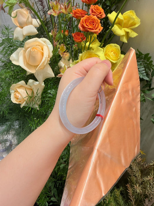 Icy light blue slim oval jadeite bangle held up in hand.